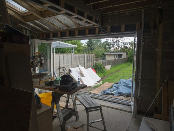 Blick durch eine offene Tür auf einen Garten mit Baumaterialien und einer Baustelle.