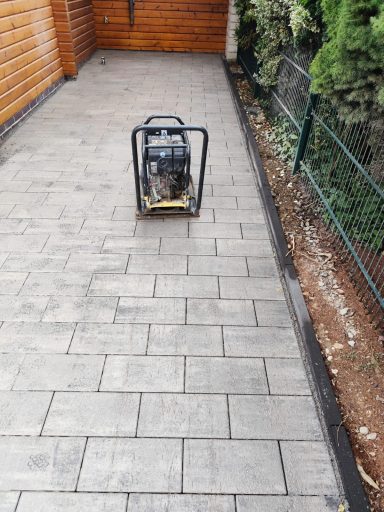 Generator auf einem gepflasterten Gartenweg, umgeben von Pflanzen und einem Holzzaun.